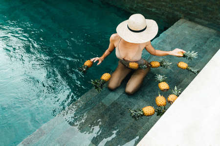 Beautiful Woman Relaxing In Swimming Pool With Pineapples. Healthy Lifestyle, Nutrition, Diet. Summer Vacationの写真素材