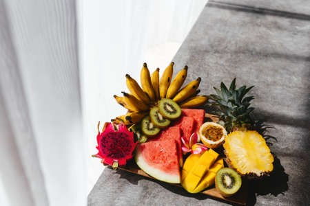 Tropical fruits assortment on a wooden plate. Stone background.の写真素材