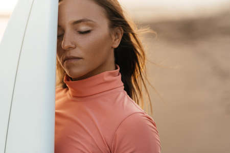 Beautiful surfer girl on the beach at sunset