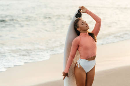 Young attractive surfer woman with white board at sunset on the ocean. Bali Indonesia.の写真素材