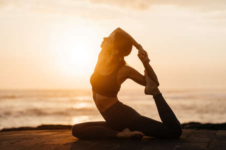 Yoga at sunset on the beach. woman performing asanas and enjoying life on the oceanの写真素材
