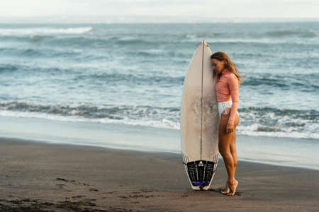 Young attractive surfer woman with white board at sunset on the ocean. Bali Indonesia.の写真素材