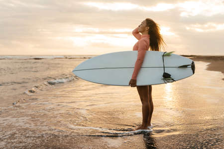 Young attractive surfer woman with white board at sunset on the ocean. Bali Indonesia.の写真素材