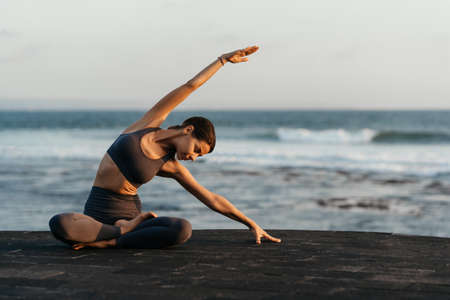 Young woman doing yoga asana in the nature with the ocean view.