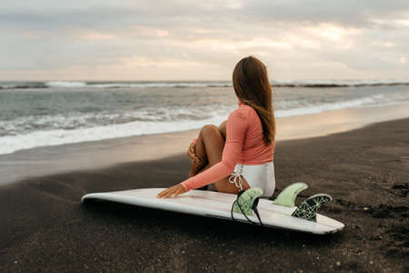 Young attractive surfer woman with white board at sunset on the ocean. Bali Indonesia.の写真素材