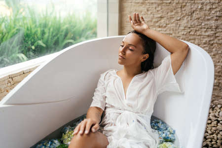 Woman relaxing in bath with tropical blue hydrangea.