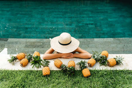 Young attractive woman by the pool enjoying delicious ripe tropical pineapple.の写真素材