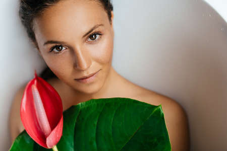 Portrait of a young woman with anthurium flower lying in tropic bath.