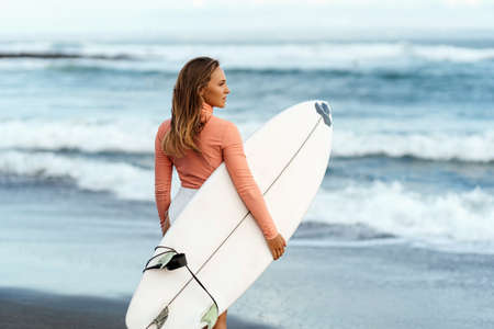 Young attractive surfer woman with white board at sunset on the ocean