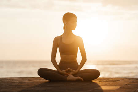 Yoga at sunset on the beach. woman performing asanas and enjoying life on the oceanの写真素材