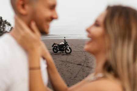 Young couple riders together on sand beach by motorbike
