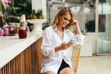Young female in casual clothes browsing smartphone in outdoor restaurantの写真素材