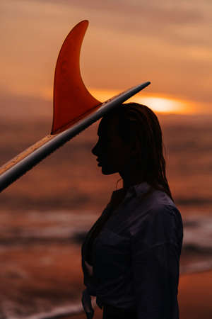 woman on tropical beach holding surfboard at sunsetの写真素材