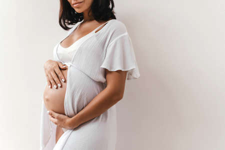 Pregnant woman holds hands on belly on a white background.の写真素材