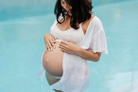 pregnant woman relax by the pool and touching her belly with handsの写真素材