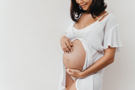 Pregnant woman holds hands on belly on a white background.の写真素材