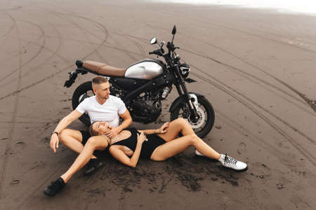 Young couple riders together on sand beach by motorbikeの写真素材