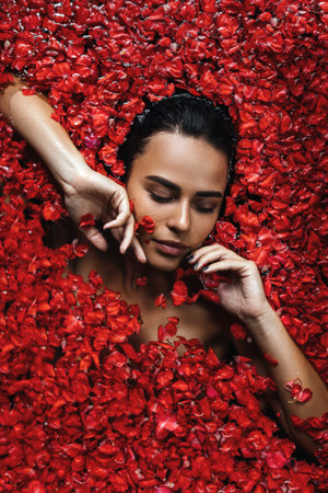 Close-up, top view, beauty portrait, face of a young woman in a bath with water and floating red rose petals and rosebuds.の写真素材