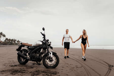 Young couple riders together on sand beach by motorbikeの写真素材