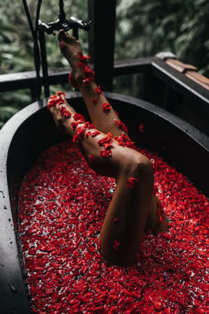 Beautiful female legs in bath with rose petal. Body care.