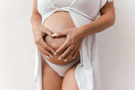 Pregnant woman holds hands on belly on a white background.