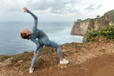 Beautiful woman doing yoga on a cliff, behind an amazing view in the oceanの写真素材