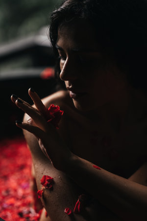 Beauty portrait, face of a young woman in a bath with water and floating red rose petals and rosebuds.の写真素材