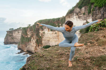 Beautiful woman doing yoga on a cliff, behind an amazing view in the oceanの写真素材
