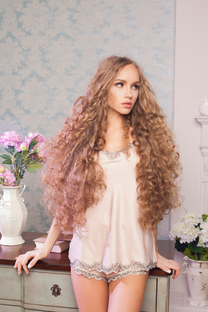 Sexy blonde woman with fashion make-up and curly hair in vintage bedroom. Skin and hair care conceptの写真素材