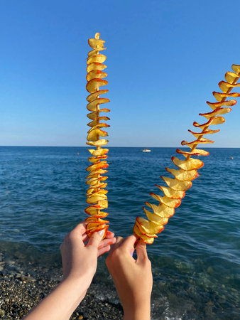 Female hands holding chips on sticks on the background of sea and blue sky