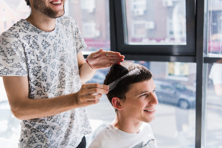 hairdresser does hair with comb of handsome satisfied client in professional hairdressing salonの写真素材