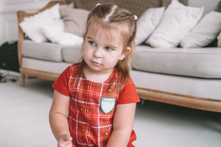 Close up little adorable thoughtful girl dreaming sitting on a floor in a living room at modern homeの写真素材