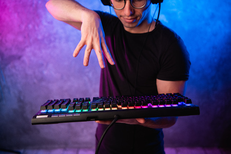 Close-up on gamers hands going to press a key on a keyboard. Background is lit with neon lightsの写真素材