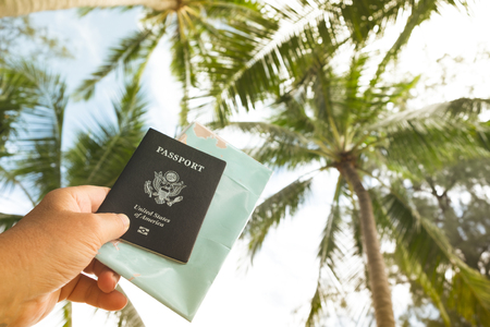 Hand holding US passport and map on sky and palm trees backgroundの写真素材