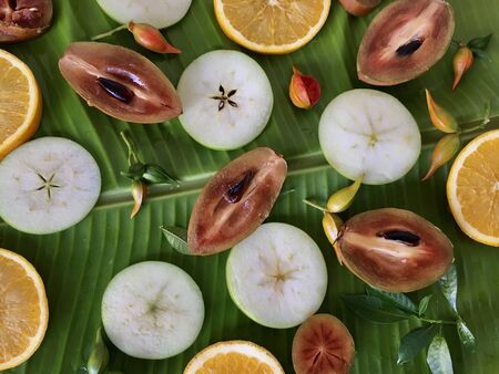 Background of fresh tropical exotic fruits on the banana leaf. Top view. Fruits sliced sapodilla, apple and orange.
の写真素材