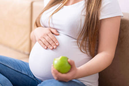 close-up of a pregnant belly and a bitten green apple in handの写真素材