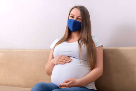pregnant woman in a blue mask sits on the couchの写真素材