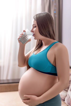 pregnant woman in sportswear drinks waterの写真素材