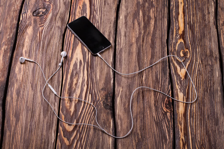 Black smart phone with headphones on old wooden desk.の写真素材