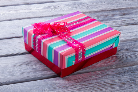 Gift box on wooden table. Colorful striped gift with pink polka dots bow. Christmas gift.の写真素材