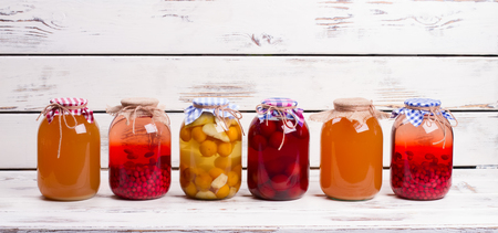 Canned fruit drinks in glass jars. Natural juices are on old wooden shelf.