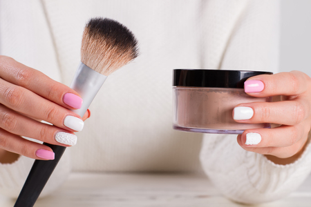 Brush with crumbly powder. Girl with delicate manicure holding cosmetics. Preparing for makeup.の写真素材
