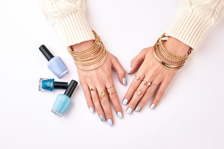Woman's manicure with blue bracelets on a white background. Different nail polishes. Blue manicure and golden bijouterie.の写真素材