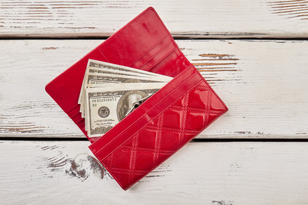 Red female purse with dollars on a wooden background.の写真素材