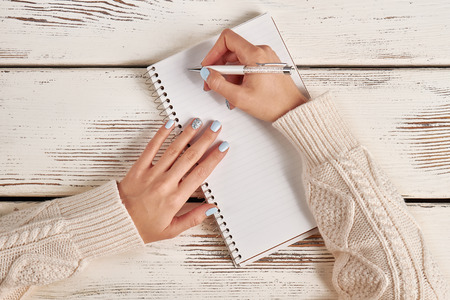 Beautiful female hand with manicure hold a pen. Writing in a notebook with a spiral. Signature on paper.の写真素材