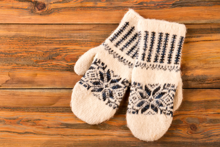 White mittens with ornament on wooden background. Winter still life. Knitted handmade woolen mittens.の写真素材