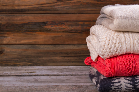 Warm knitted sweaters on a wooden background. Set of handmade pullovers. Colorful woolen sweaterの写真素材
