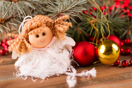 Little fairy sitting under the Christmas tree. Doll with balls and fir tree on the wooden background.の写真素材