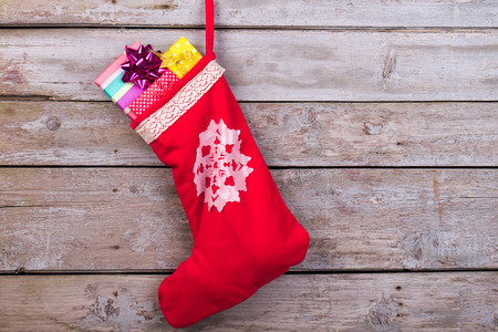 Red christmas sock with snowflakes for Santa gifts hanging on wooden background. Holidays symbol stocking.の写真素材