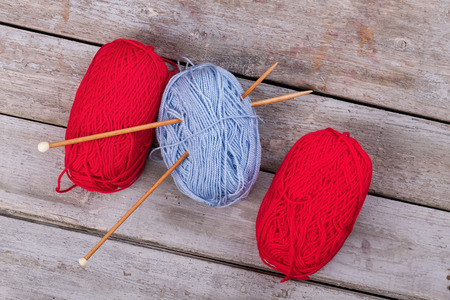 Red and blue yarn with wooden knitting needles. Skein of threads on vintage wooden background.